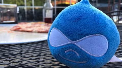 Stuffed Drupal icon on a table with pizza and bottle in background.