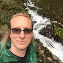 Woman with green hair smiling in front of a waterfall
